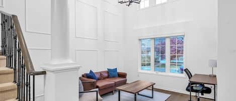 A spacious room with a staircase, a brown leather sofa with blue cushions, a wooden coffee table, and a desk with a chair.