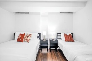 Ein Hotelzimmer mit zwei Betten, jeweils mit Kissen und einem Nachttisch mit Lampe.