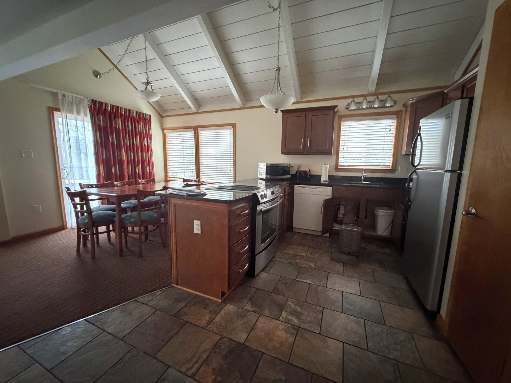 A kitchen with a central island, wooden cabinets, a refrigerator, and a microwave.