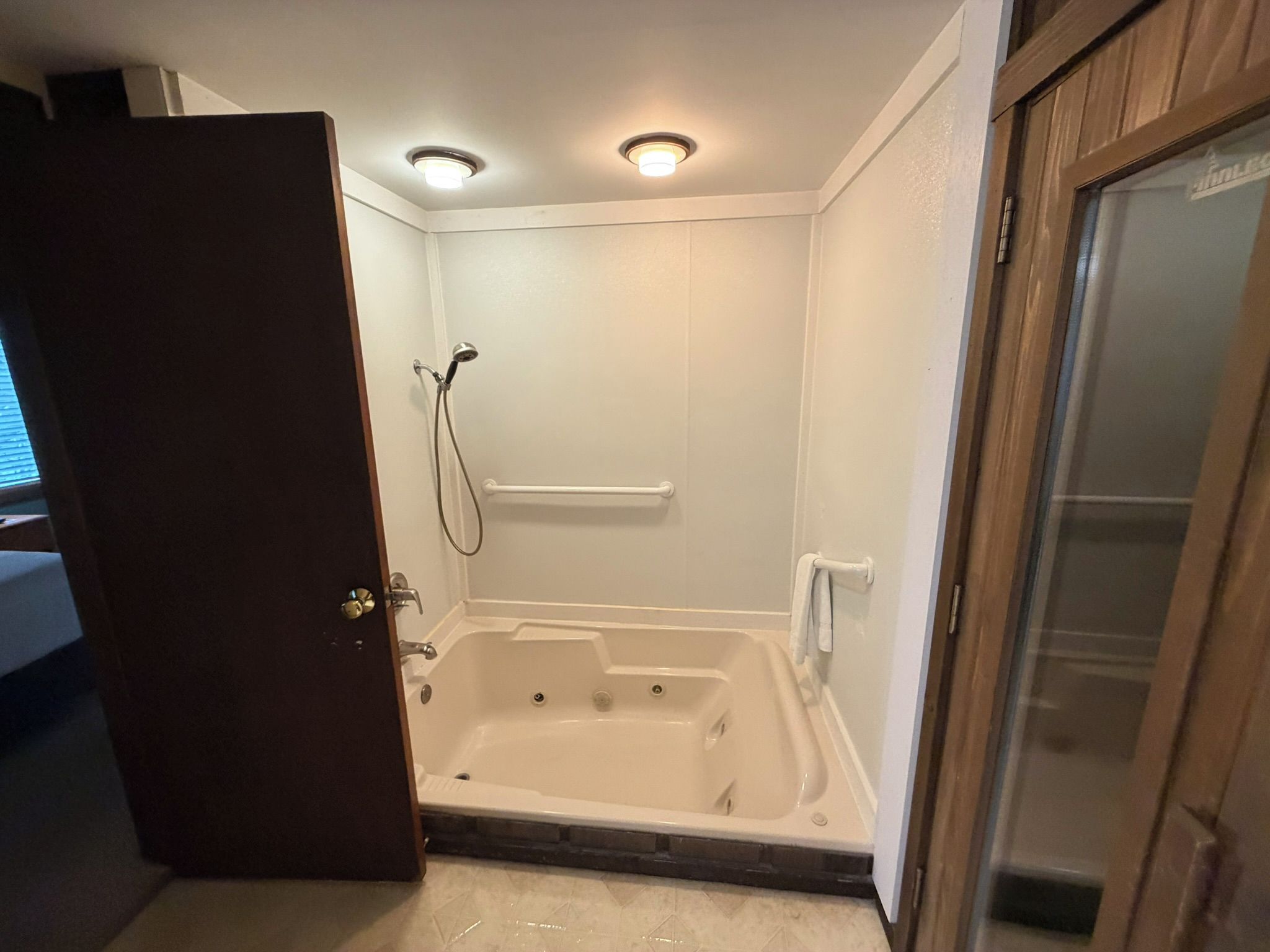 A corner bathroom with a walk-in shower, a bathtub, and a door leading to another room.