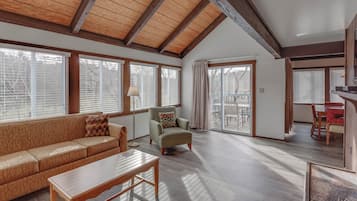 A spacious living room with a high ceiling, wooden beams, a sofa, a chair, and a dining area with a table and chairs.