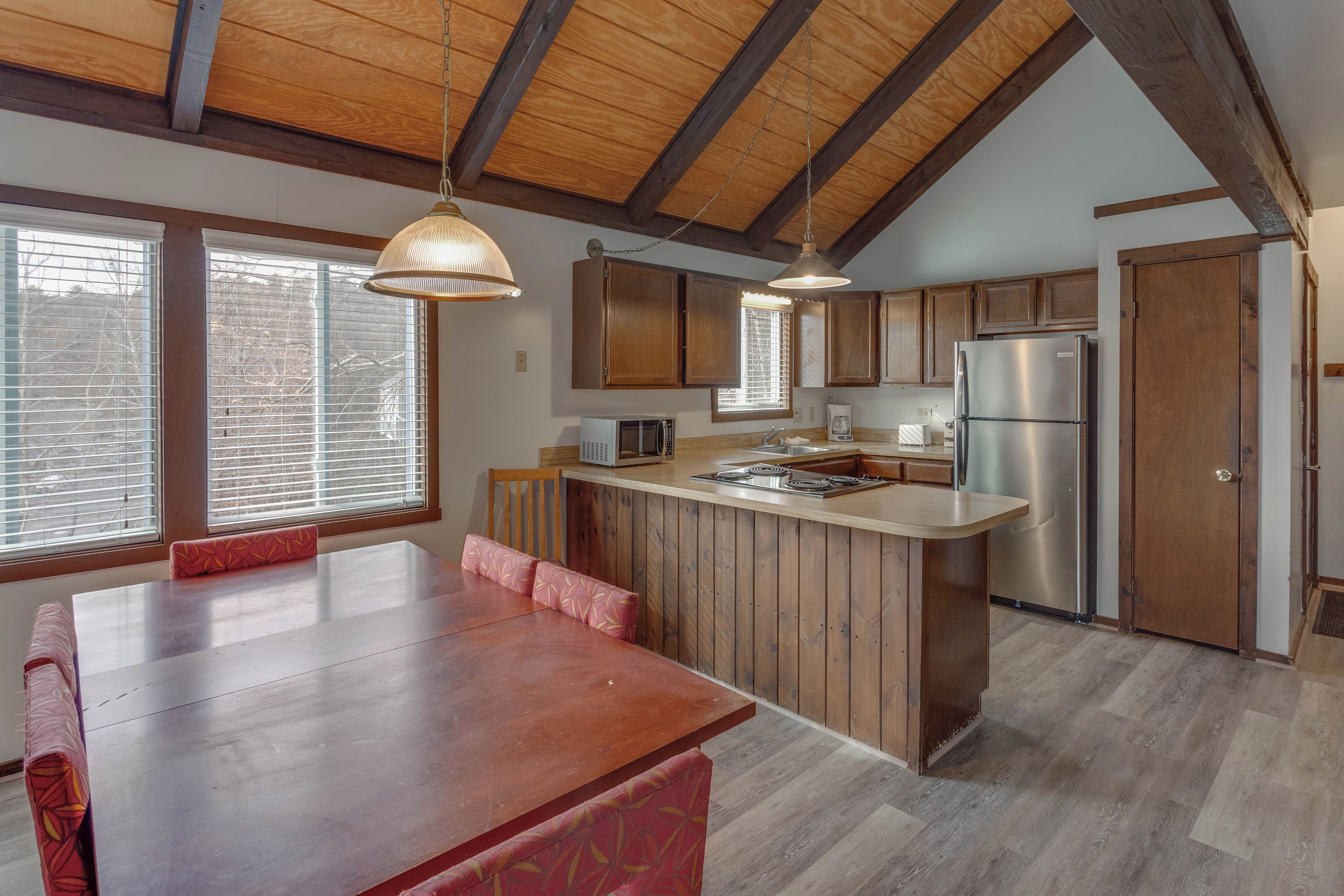 A modern kitchen with wooden cabinets, a stainless steel refrigerator, and a dining area with a wooden table and chairs.