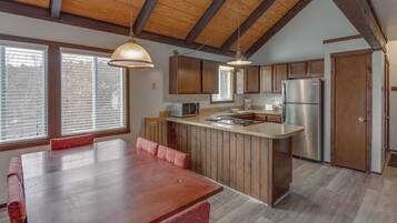 A modern kitchen with wooden cabinets, a stainless steel refrigerator, and a dining area with a wooden table and chairs.