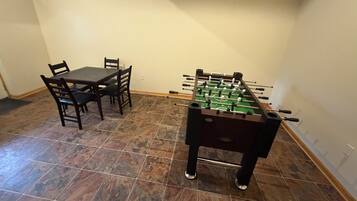 Een kamer met een tafelvoetbaltafel en een eettafel met stoelen.