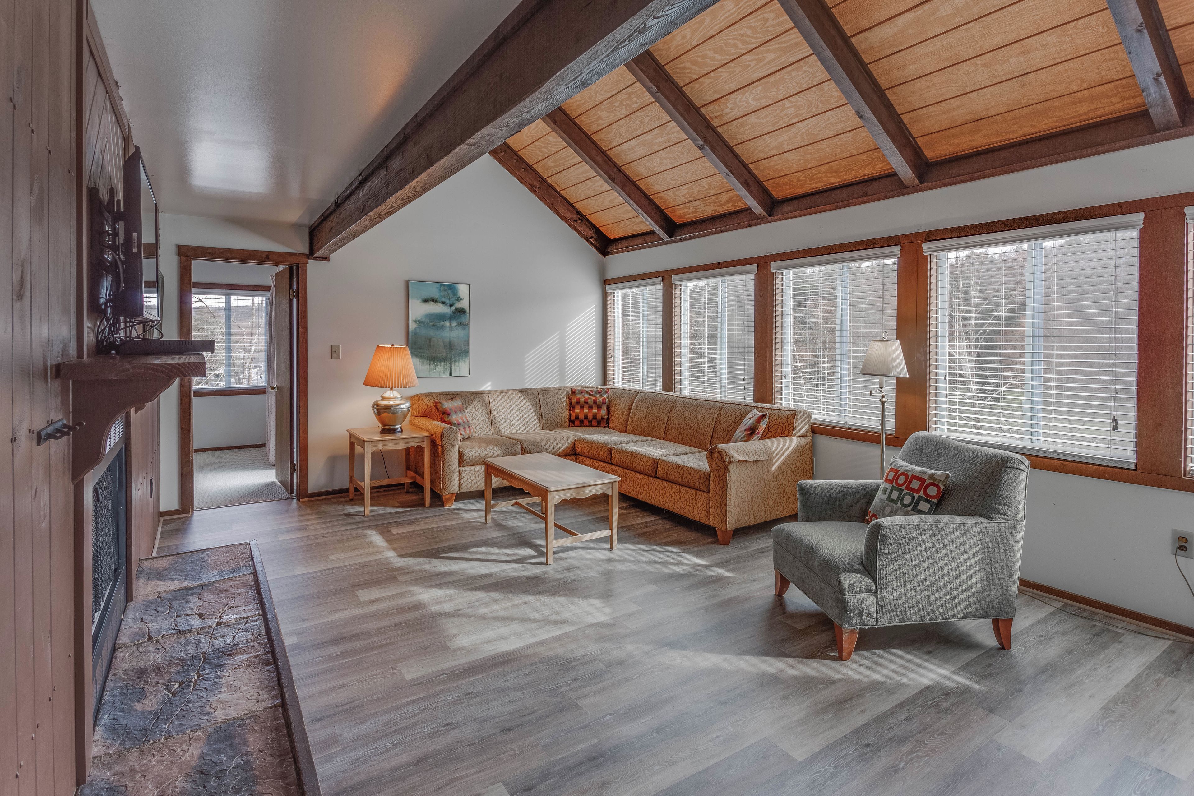 A spacious living room with a high ceiling, wooden beams, a sofa, a coffee table, and a fireplace.