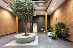 Ein modernes Interieur mit einem zentralen Baumbeet, einer Ziegelwand und einer Tür mit der Aufschrift 'APT102-106'.