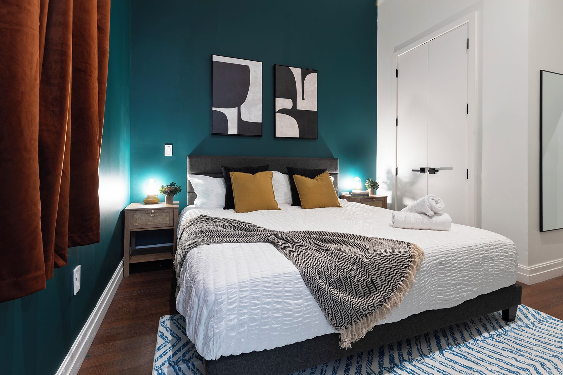 Une chambre à coucher avec un lit, des tables de chevet, une lampe fixée au mur et une porte.