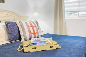 Ein Bett mit blauer Tagesdecke, ein gestreiftes Kopfkissen mit Anker-Motiv und eine kleine Holzkiste mit Reiseführer und Karte.