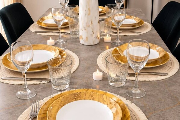 Una mesa de comedor dispuesta con platos de borde dorado, cristalería transparente y un centro de mesa de mármol.