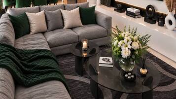 A modern living room with a grey sectional sofa, a round coffee table with a candle, and a vase with white flowers.