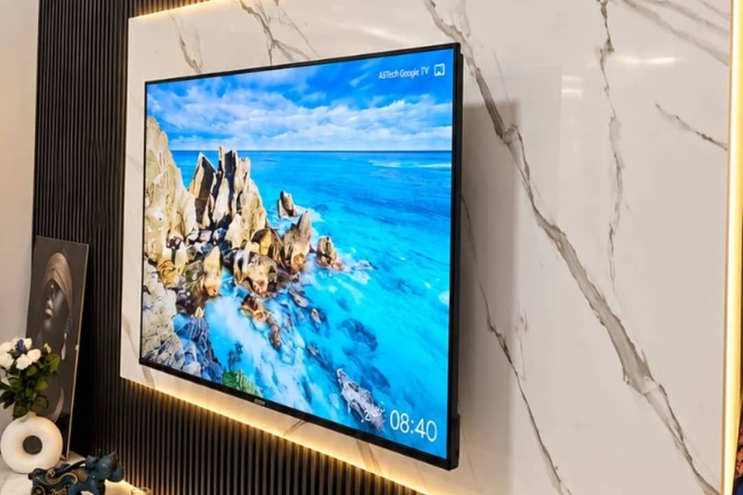 A flat-screen TV mounted on a wall with a marble-like texture, displaying a scenic coastal image.