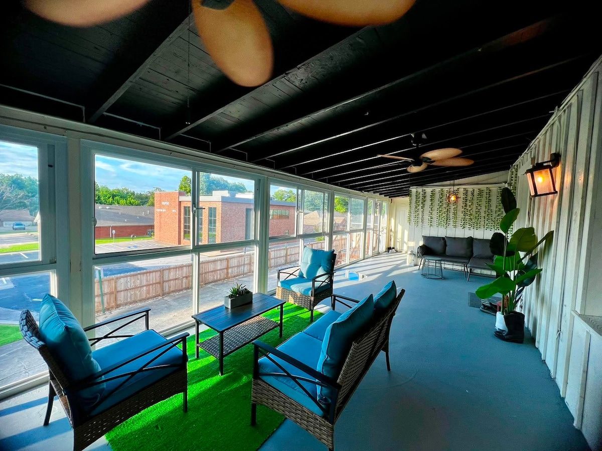 A covered outdoor seating area with wicker furniture and a green artificial turf.