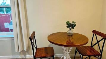 Une table ronde en bois, accompagnée de deux chaises, un vase avec une plante et une fenêtre avec des rideaux.