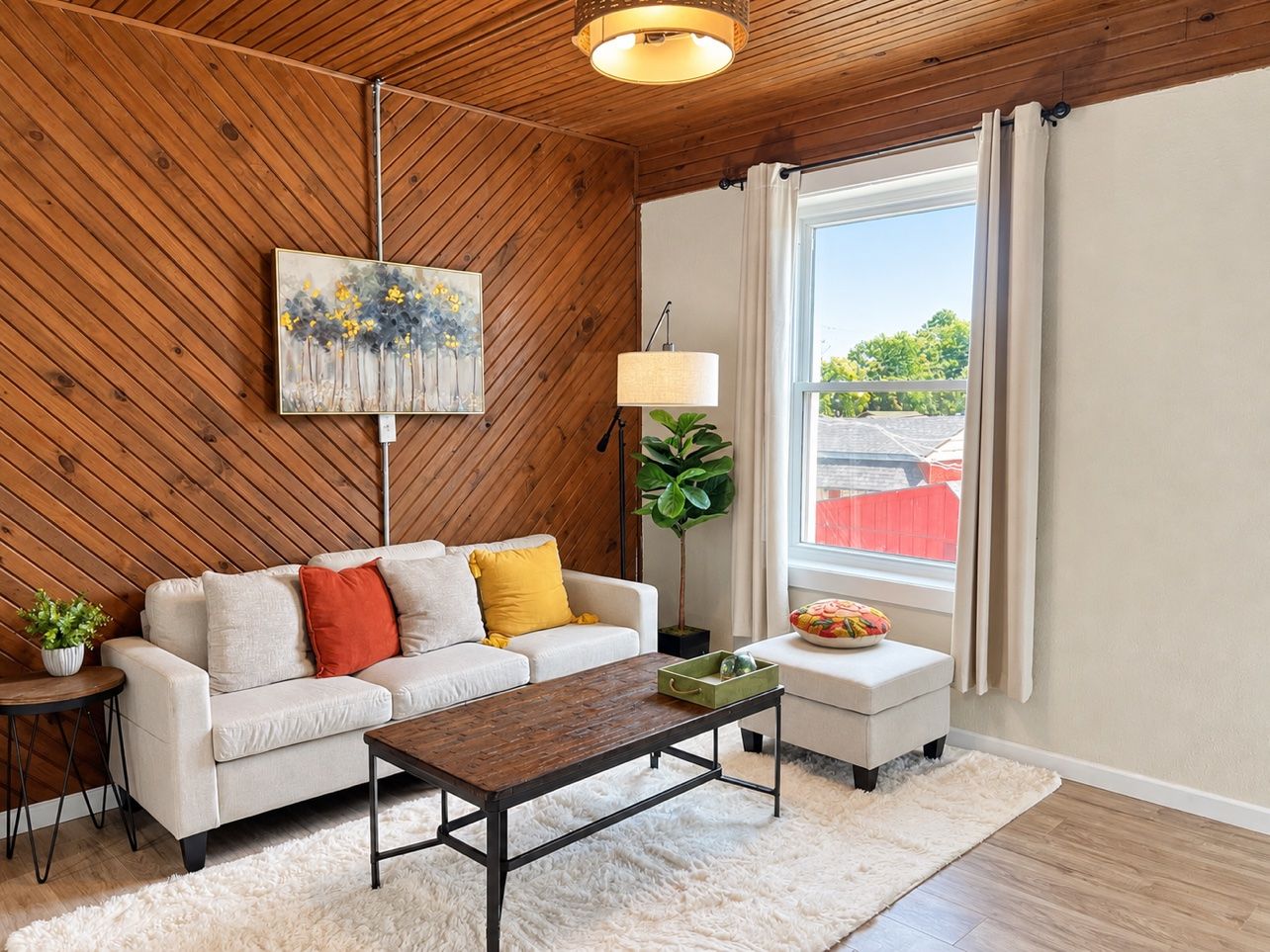A living room with a wooden ceiling, a sofa, a coffee table, a floor lamp, a painting, and a window with curtains.