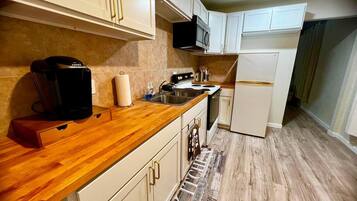 A kitchen with white cabinets, a wooden countertop, a microwave, a coffee maker, and a stainless steel sink.