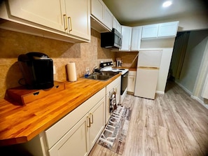 A kitchen with white cabinets, a wooden countertop, a microwave, a coffee maker, and a stainless steel sink. - Suite 1: Boutique 1BR + Full Kitchen - Sleeps 3 (Fort Smith)