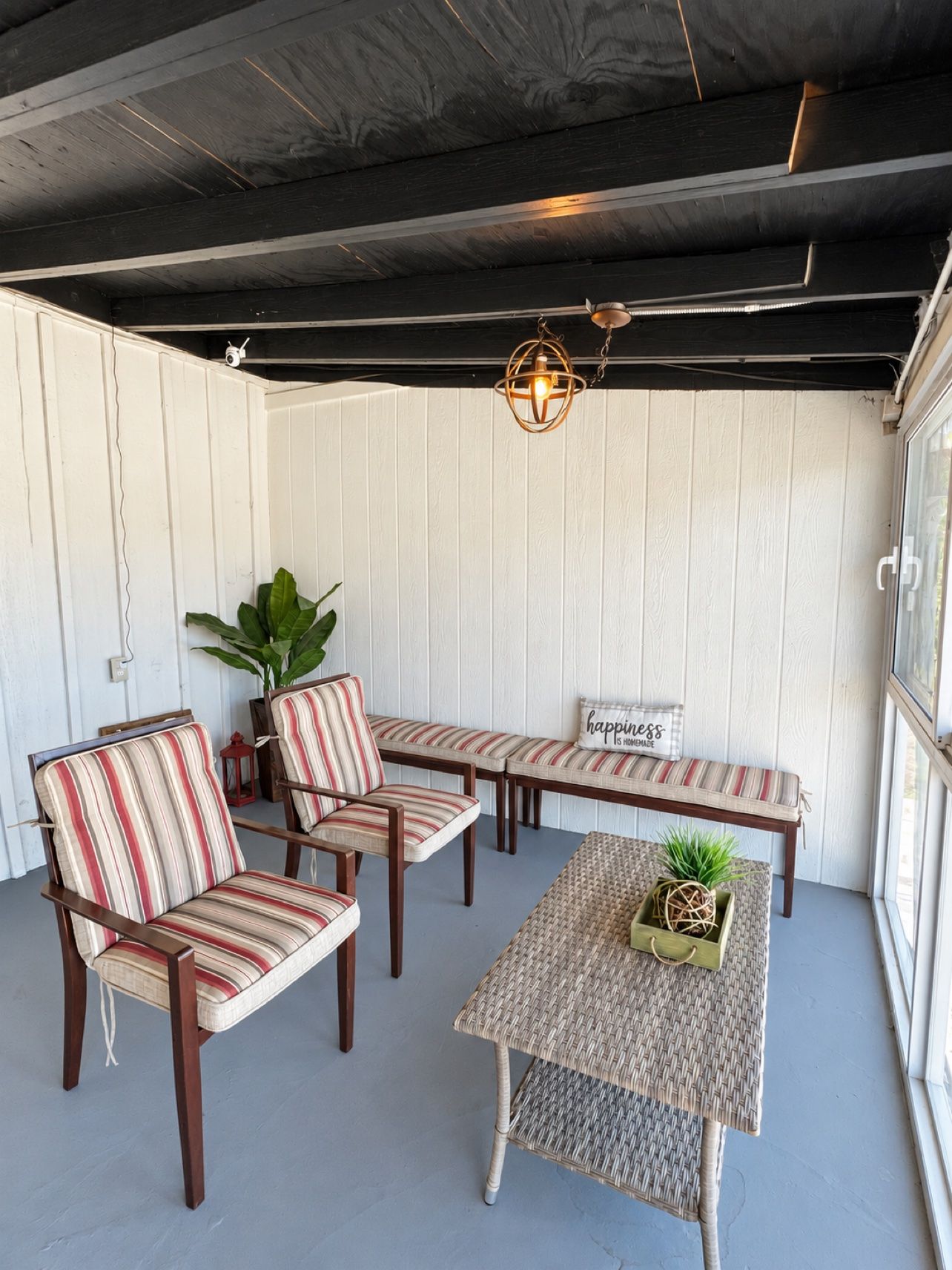 A covered patio with striped chairs and a woven table, a hanging light fixture, and a potted plant.