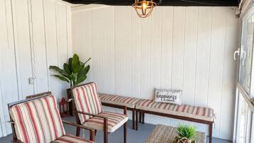 A covered patio with striped chairs and a woven table, a hanging light fixture, and a potted plant.