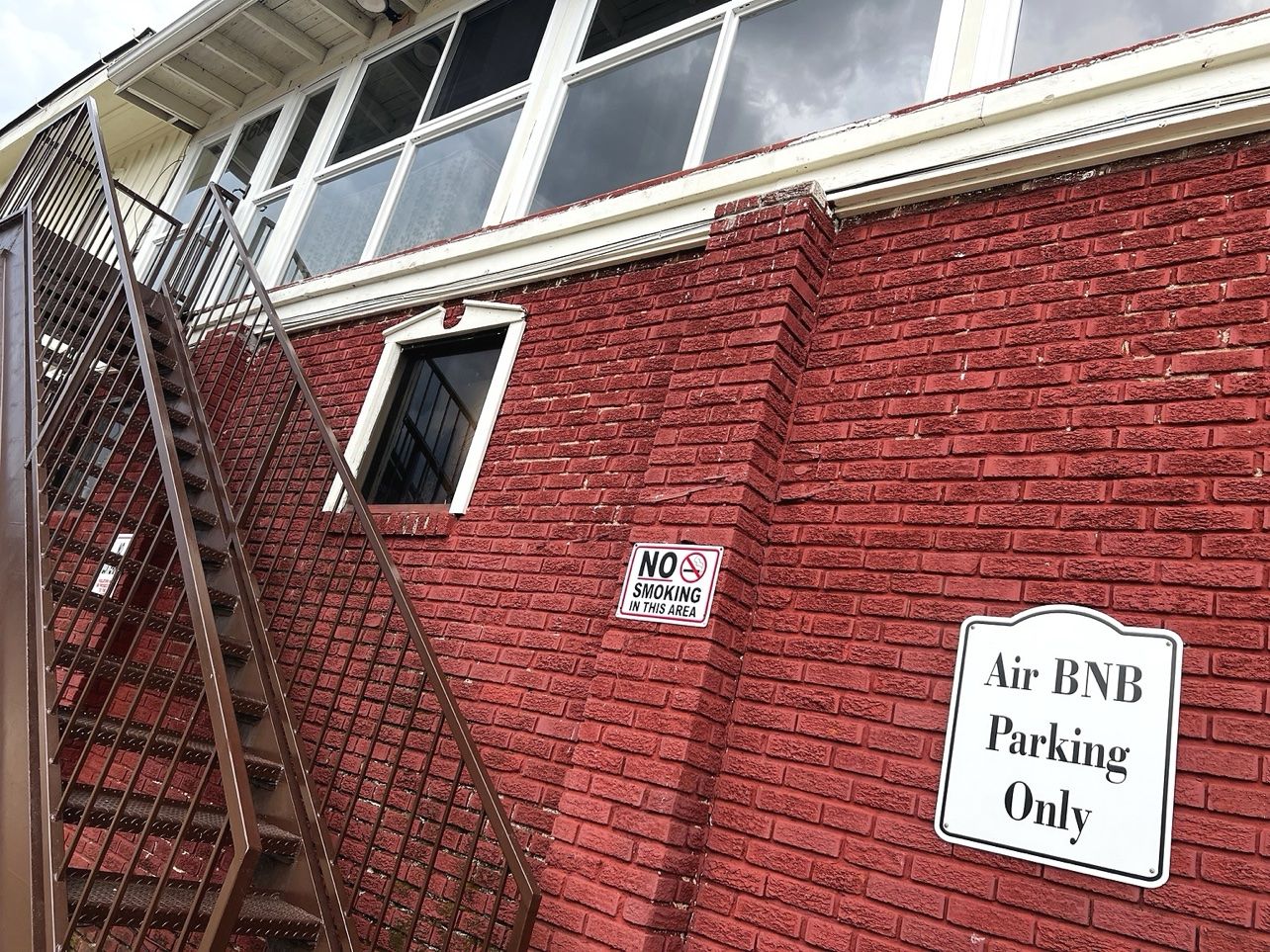 A red brick building with a fire escape, a no smoking sign, and an Air BNB parking sign.