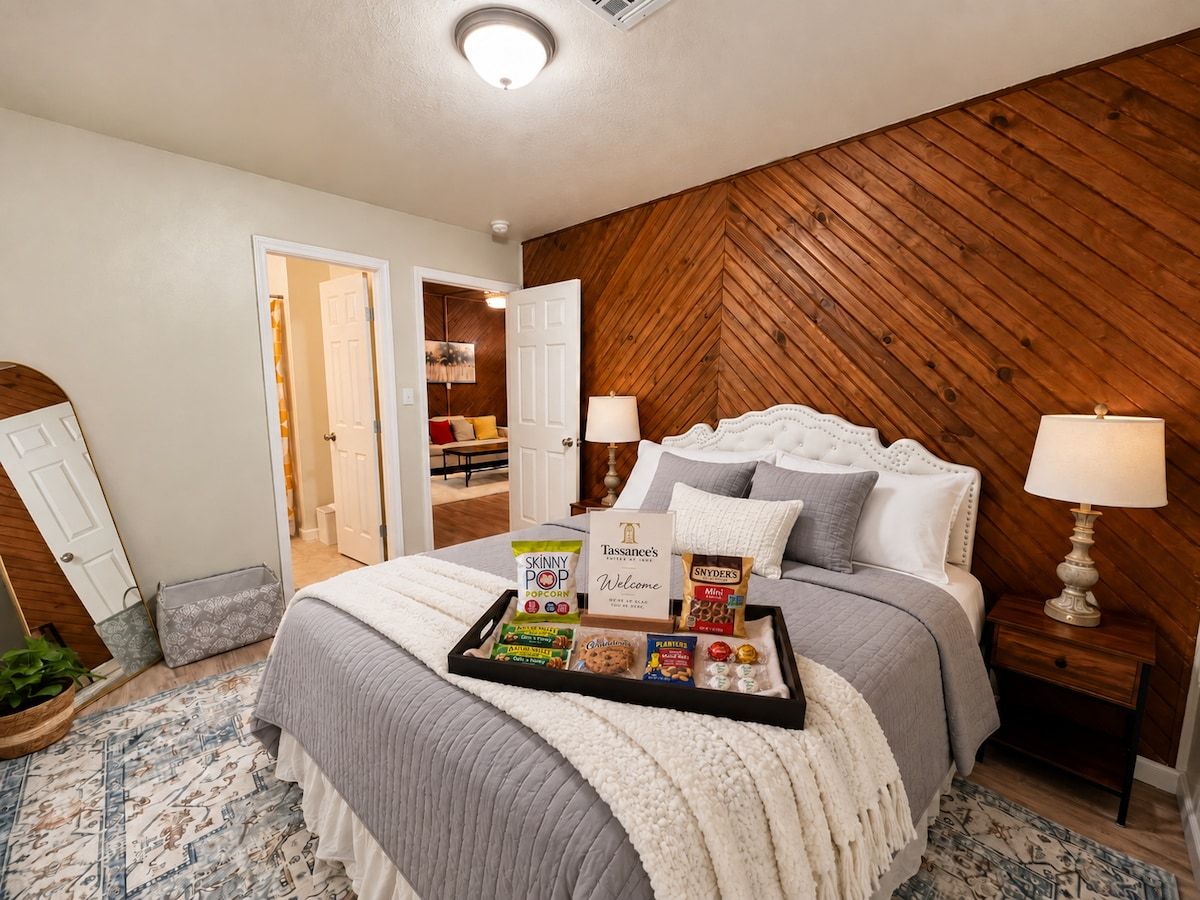 A bedroom with a bed, bedside tables, a tray with snacks, and a door leading to another room.