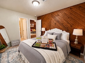 A bedroom with a bed, bedside tables, a tray with snacks, and a door leading to another room. - Suite 1: Boutique 1BR + Full Kitchen - Sleeps 3 (Fort Smith)
