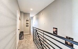 A hallway with a carpeted floor, a bench, a wall-mounted light fixture, and a railing. - Elegant 3BR Townhome with Private Yard & 2-Car Garage (Houston)