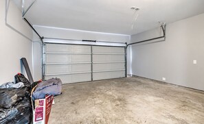 A garage with a closed garage door, concrete floor, and a metal ladder leaning against the wall. - Elegant 3BR Townhome with Private Yard & 2-Car Garage (Houston)