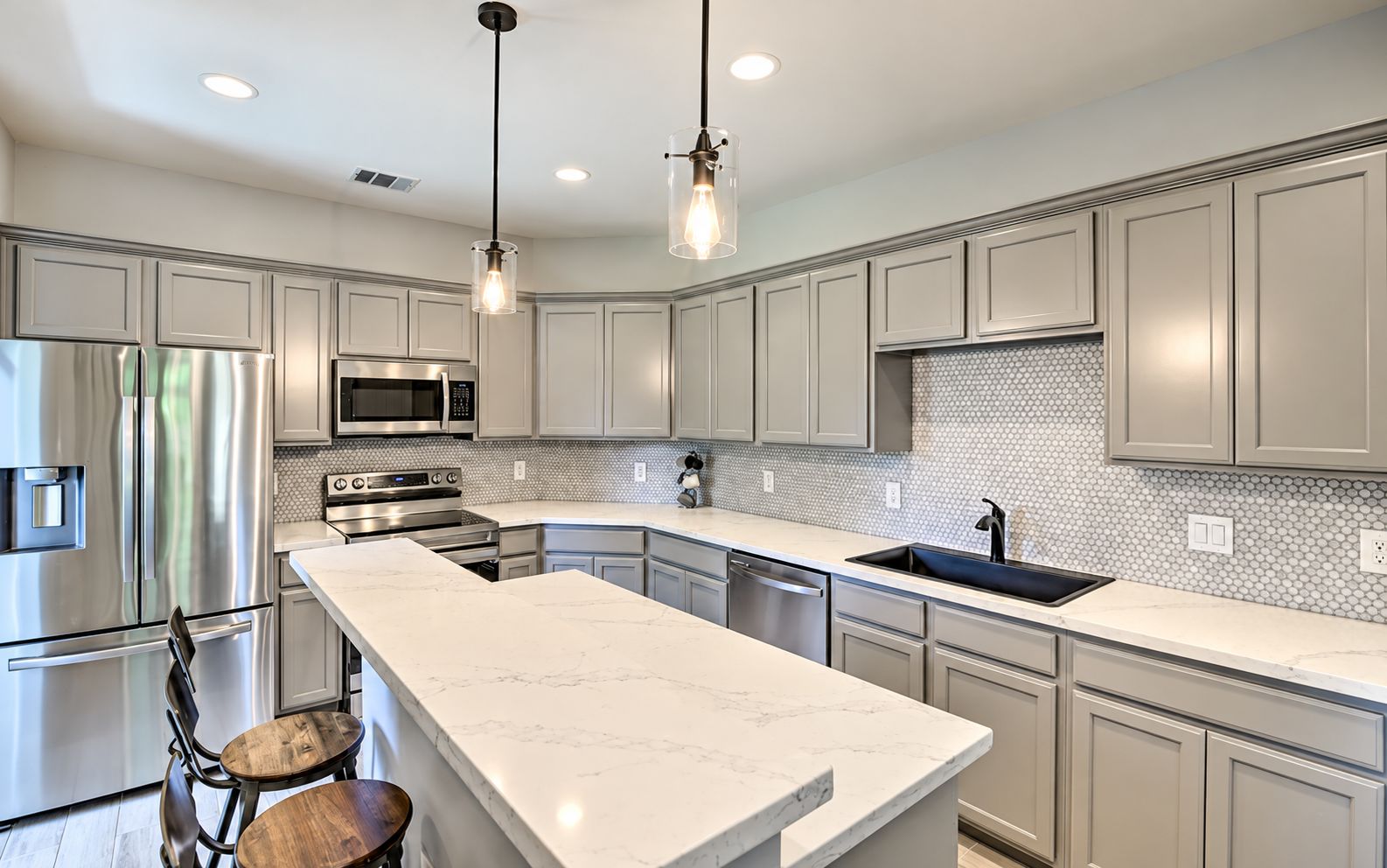 A modern kitchen with stainless steel appliances, a marble countertop, and pendant lighting.
