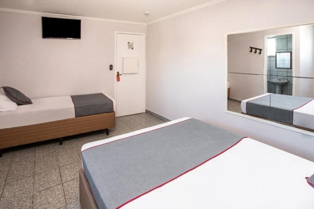 Et hotelværelse med en seng, et natbord, et spejl og et fjernsyn på væggen.