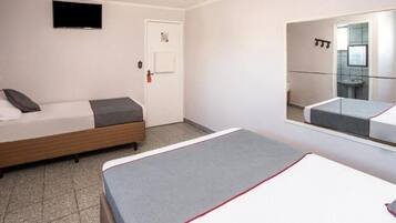 Et hotelværelse med en seng, et natbord, et spejl og et fjernsyn på væggen.