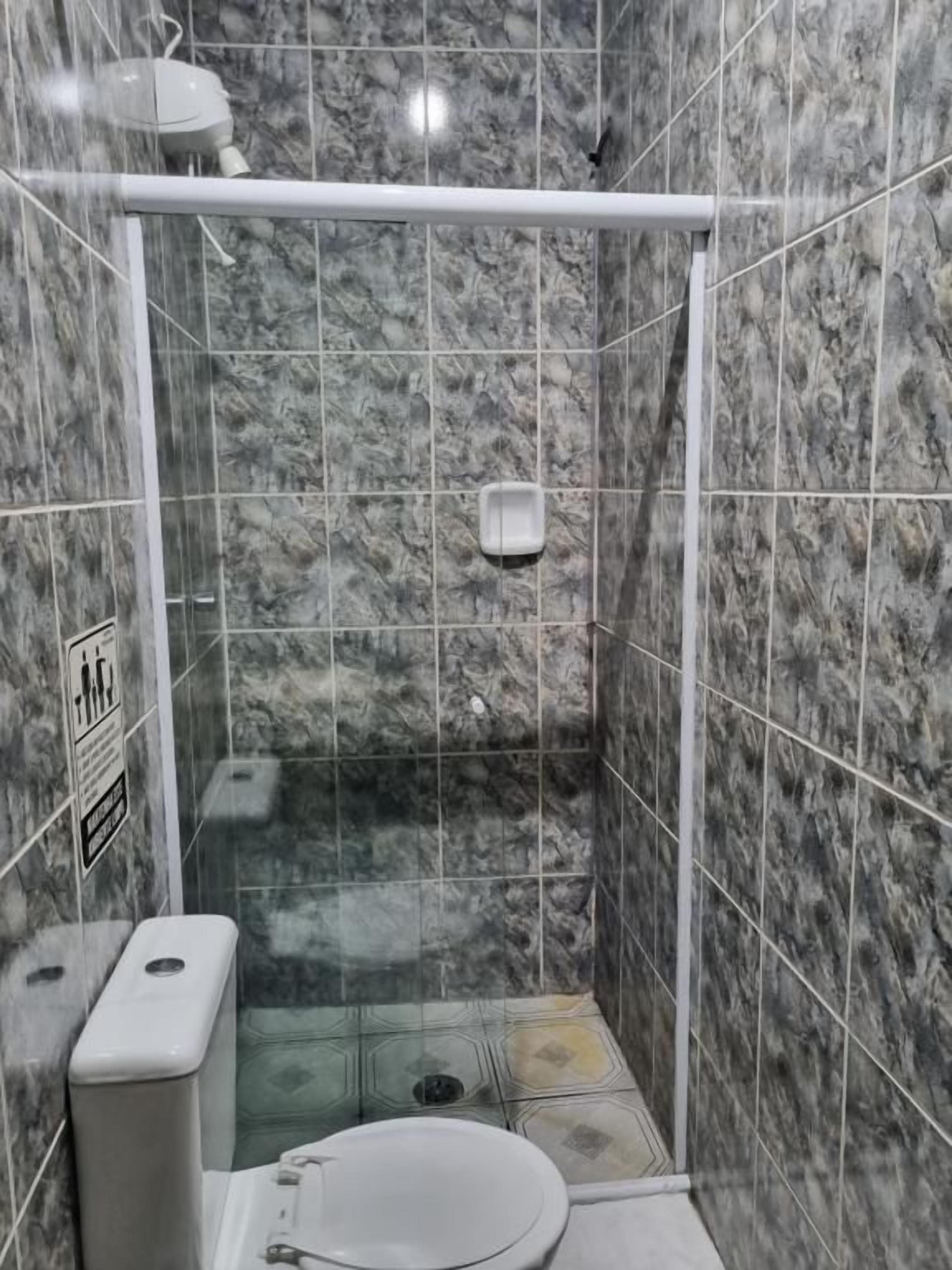 Une petite cabine de douche fermée, équipée de toilettes et d’un distributeur de savon liquide.