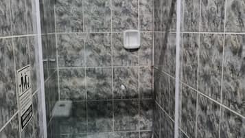 Une petite cabine de douche fermée, équipée de toilettes et d’un distributeur de savon liquide.