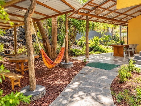 A covered outdoor area with a hammock, wooden benches, and a stone pathway.