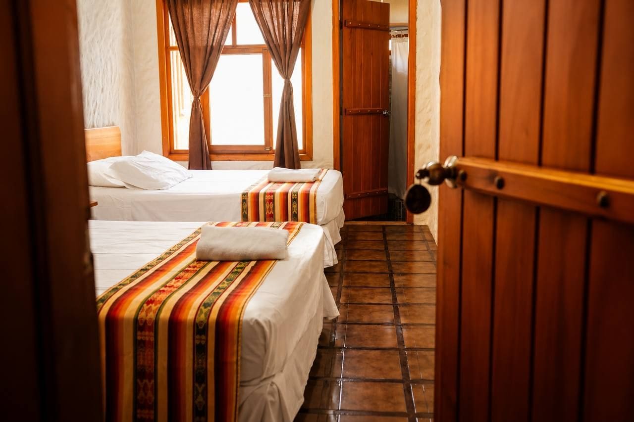 Una habitación de hotel con dos camas, una puerta de madera y piso de baldosas.