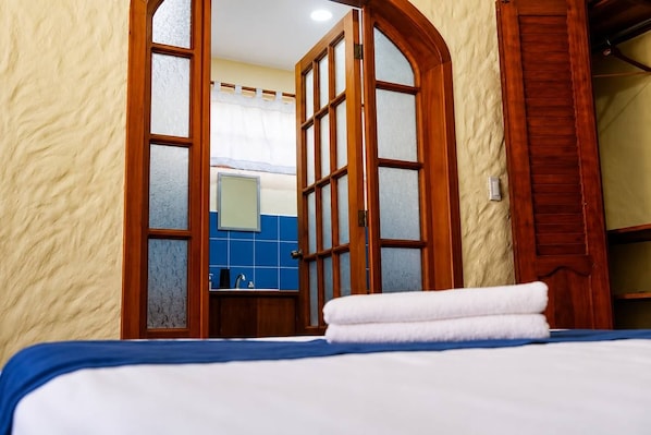 A hotel room with a bed, a wooden door with glass panels, a bathroom with a sink, and a blue tiled wall.
