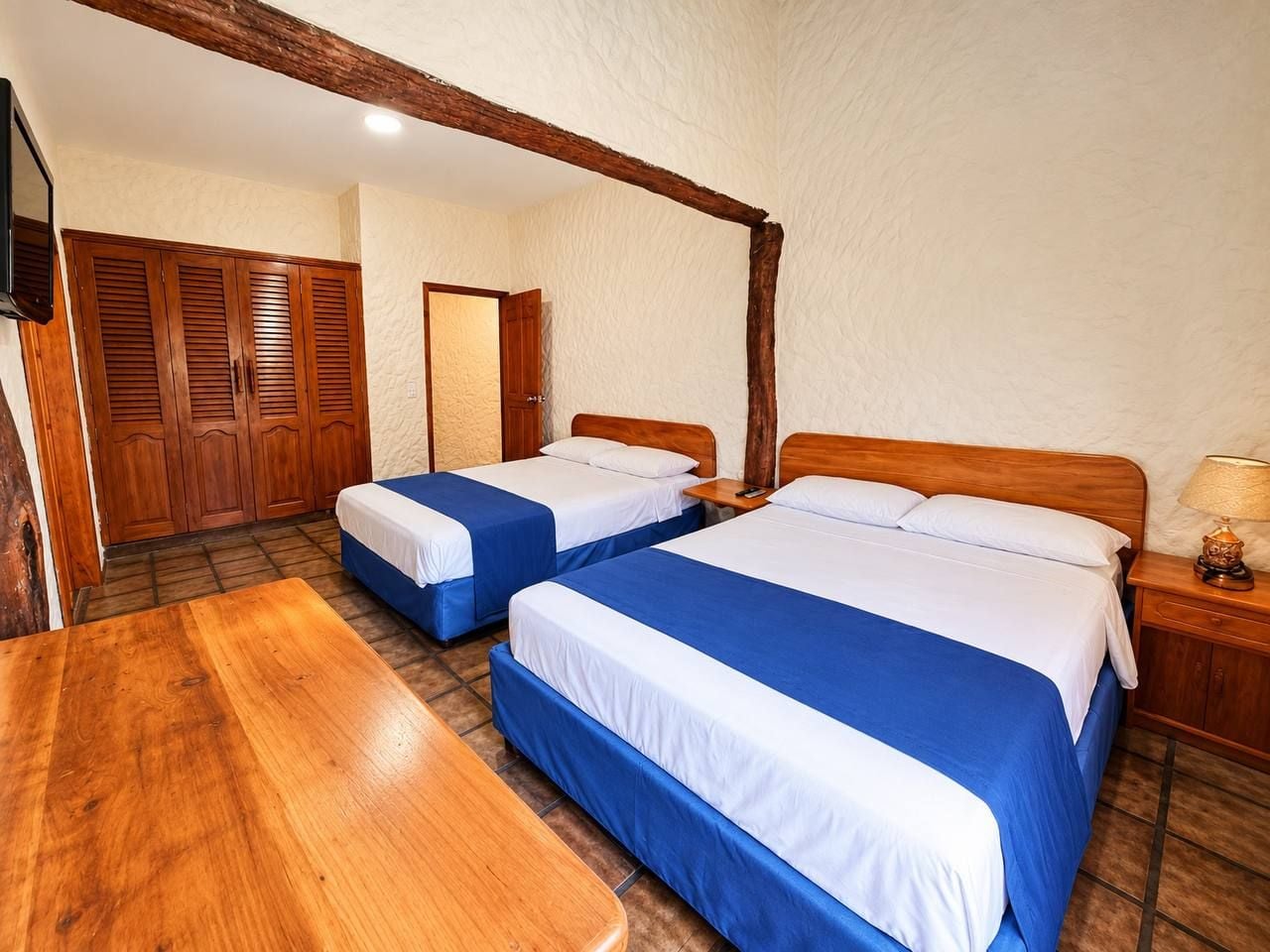 A room with two beds, a wooden table, and a wardrobe.