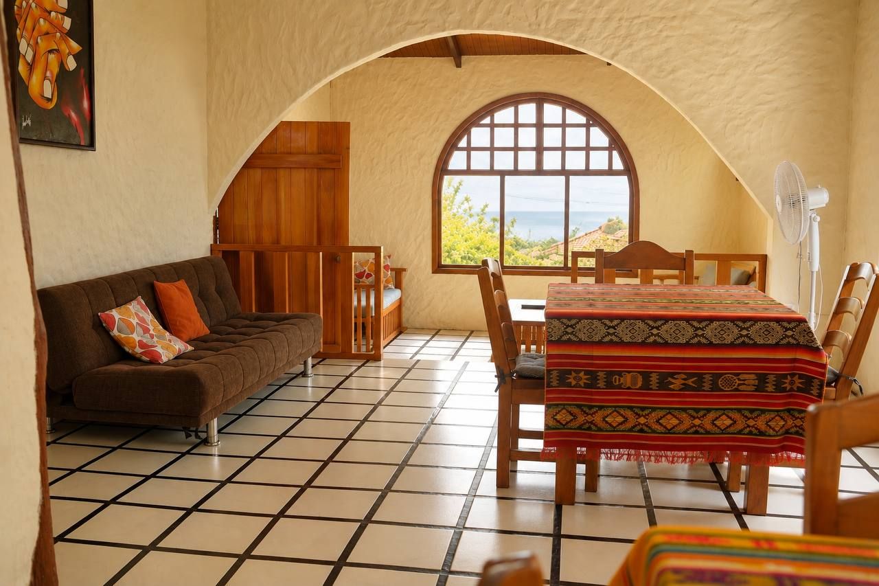 A room with a tiled floor, a sofa, a dining table with chairs, and a large arched window.