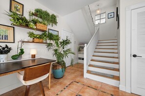 Una escalera con paredes blancas y barandilla de madera, que conduce a una habitación con un escritorio y estantes llenos de plantas.