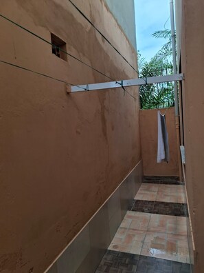 Ein schmaler Korridor mit Fliesenboden, einer Wäscheleine und einem kleinen Fenster.