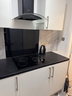 A modern kitchen with a black stovetop, white cabinets, and a glass hood. - Beautiful spacious 2 bedroom apartment, 5 minutes from Heaton park. (Manchester)