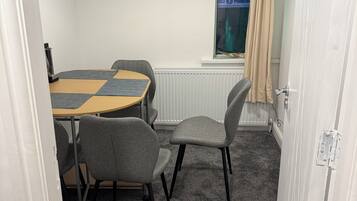 A room with a round table and four chairs, a radiator, a window with a curtain, and a door.