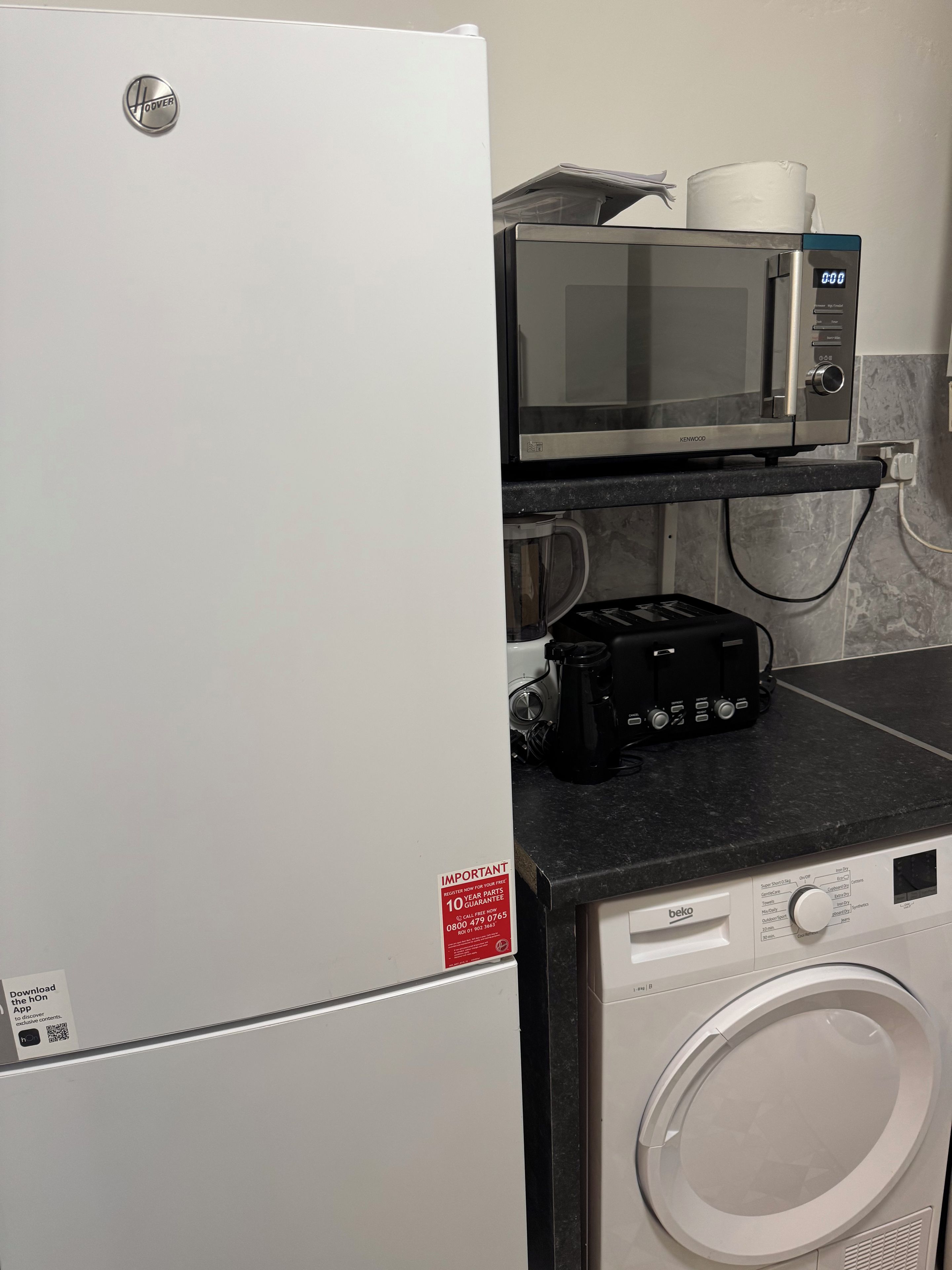 A kitchen with a white refrigerator, a microwave, a coffee maker, and a washing machine.