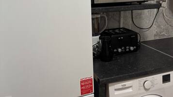 A kitchen with a white refrigerator, a microwave, a coffee maker, and a washing machine.