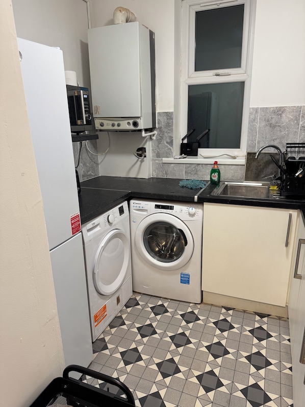 A compact kitchen with a washing machine, a microwave, and a sink. - Beautiful spacious 2 bedroom apartment, 5 minutes from Heaton park. (Manchester)