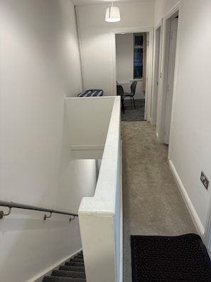 A clean, modern stairwell with a handrail, carpeted stairs, and a black doormat at the bottom. - Beautiful spacious 2 bedroom apartment, 5 minutes from Heaton park. (Manchester)