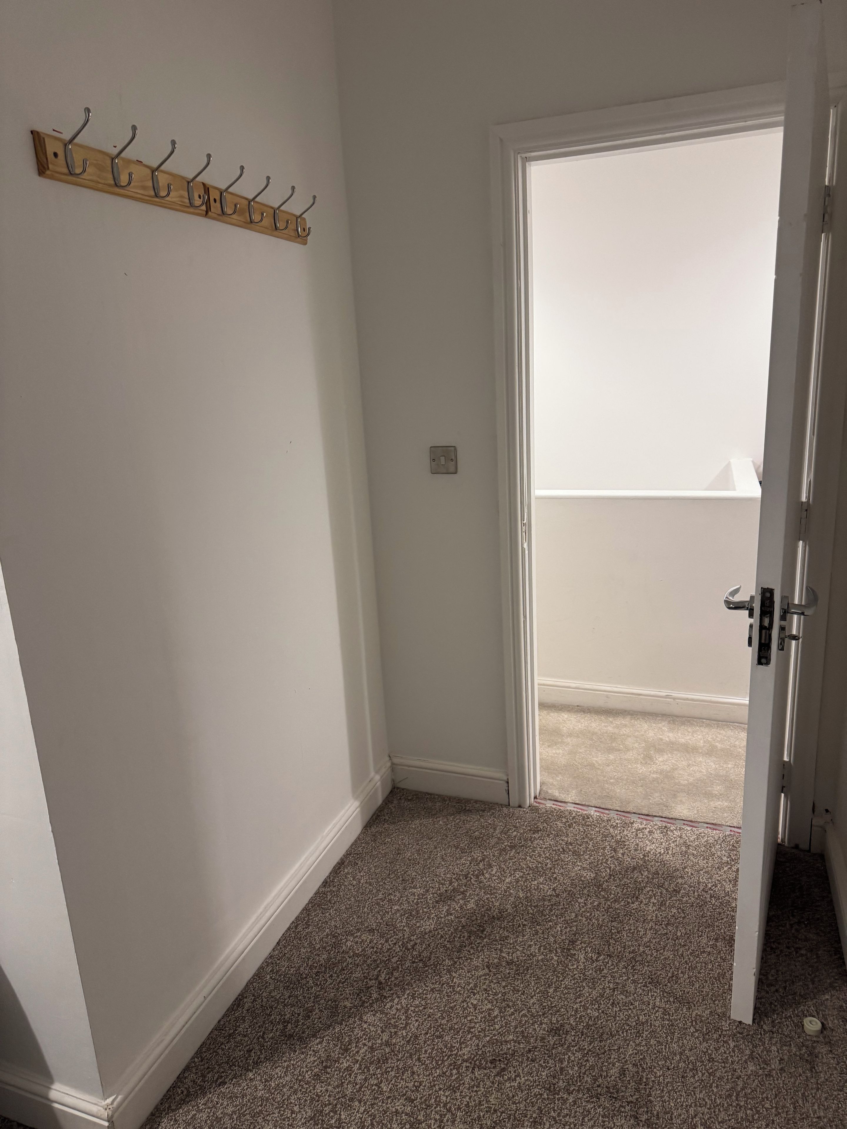 A room with a door leading to a balcony, a coat rack on the wall, and a carpeted floor.