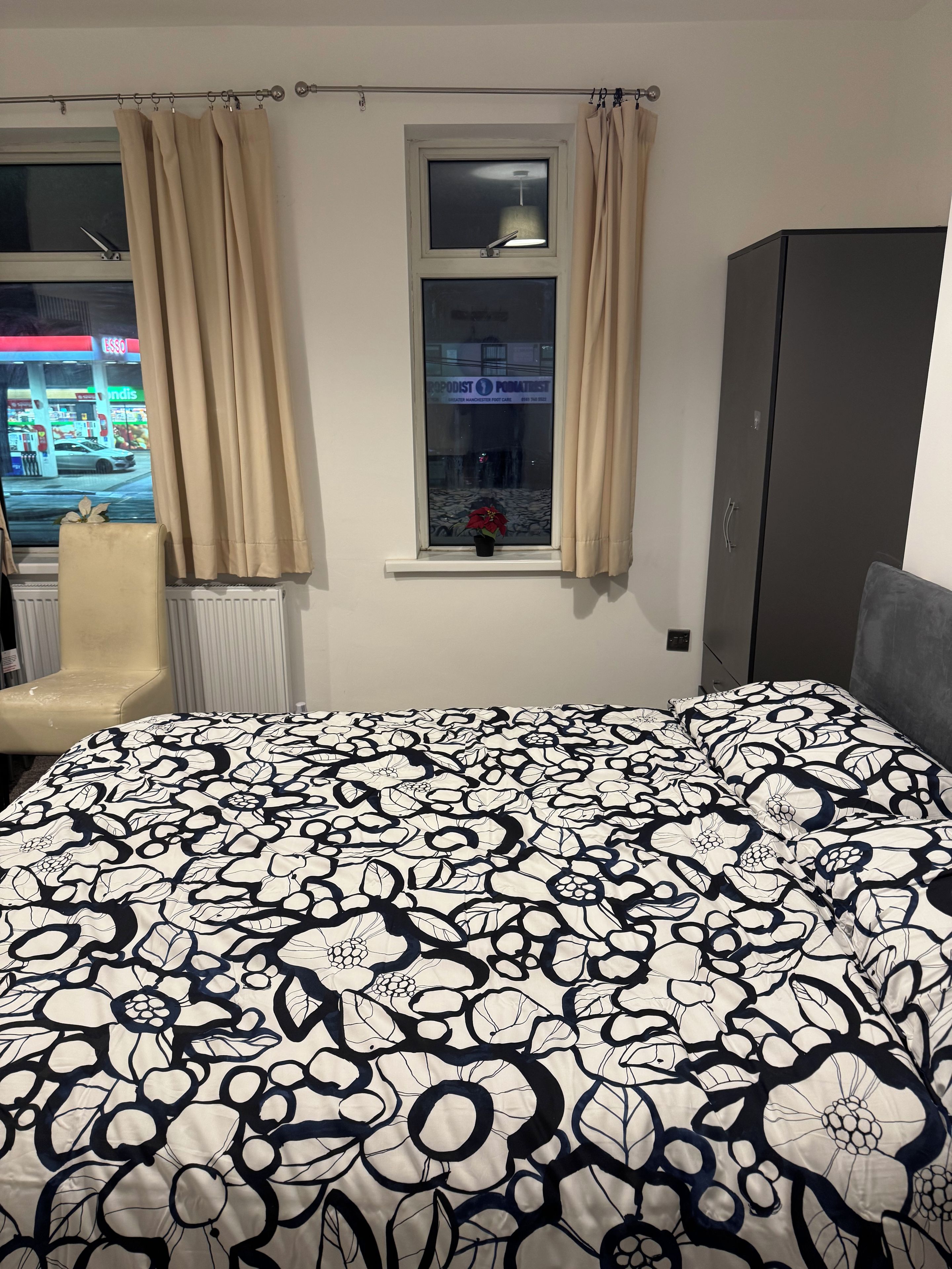 A bedroom with a bed, a window with curtains, a radiator, and a wardrobe.