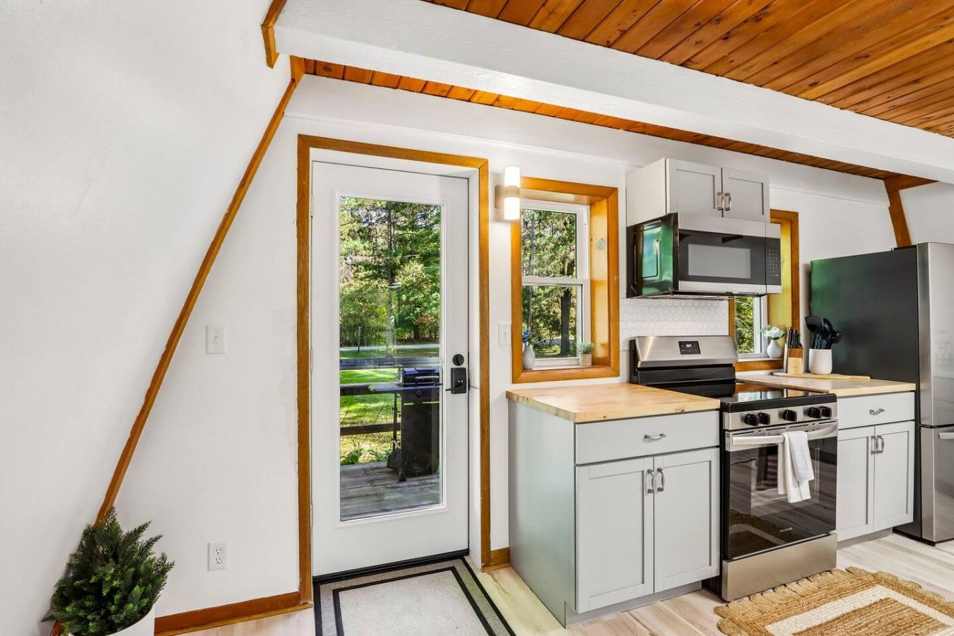 A modern kitchen with white cabinets, stainless steel appliances, and a wooden ceiling.