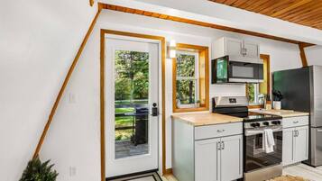 A modern kitchen with white cabinets, stainless steel appliances, and a wooden ceiling.