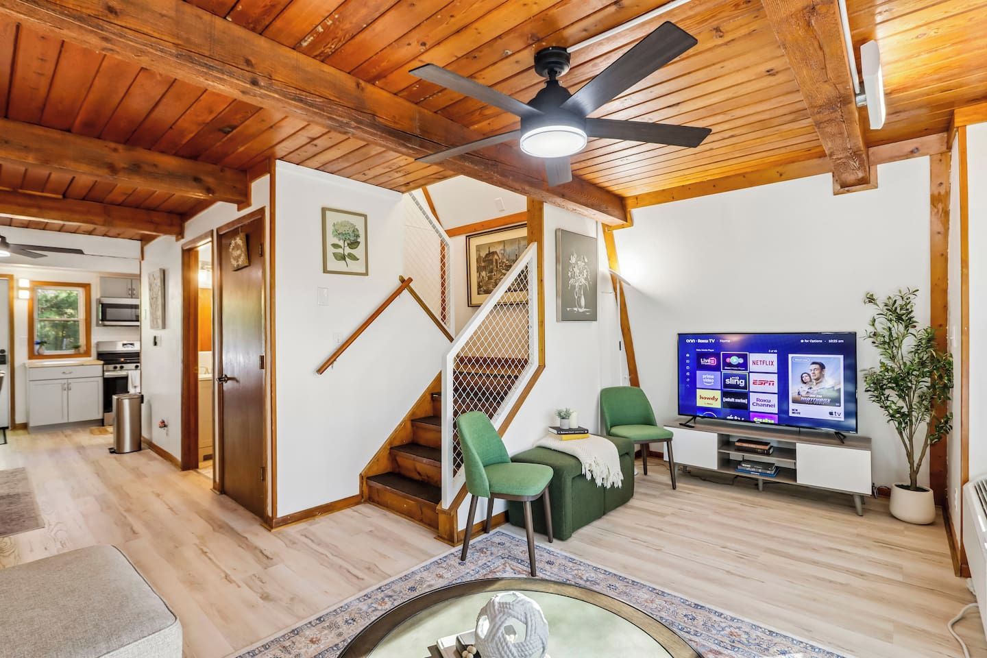 Una sala moderna con techo de madera, una escalera, un televisor de pantalla plana y un comedor.